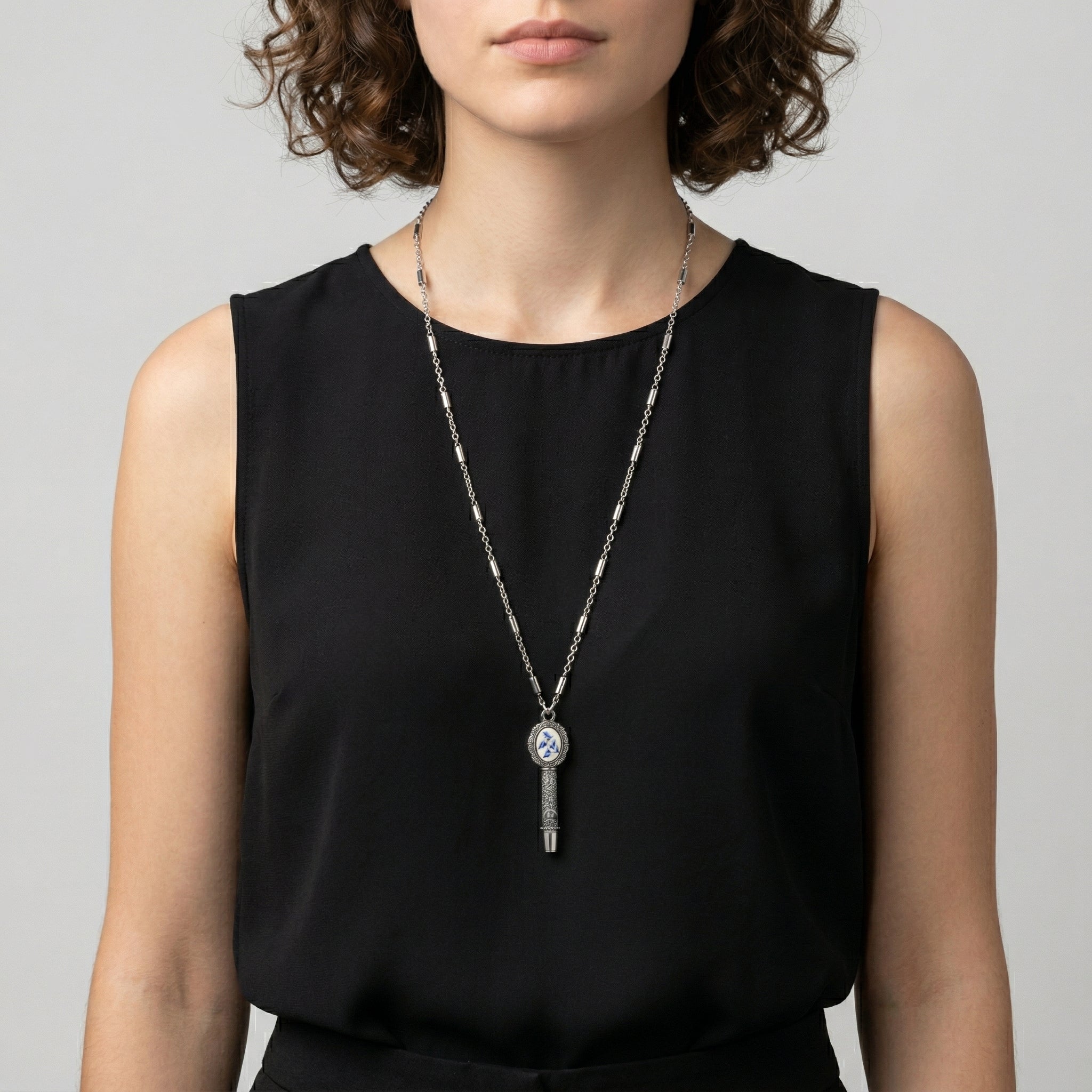 Person wearing a black sleeveless top with a long whistle pendant necklace against a neutral background