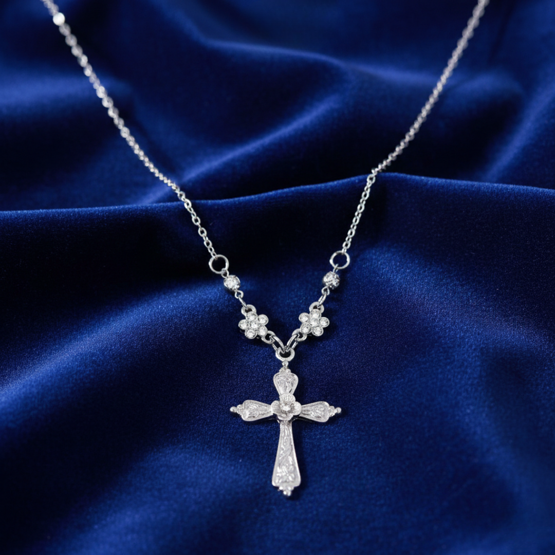Silver cross necklace with floral details on a blue fabric background