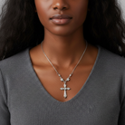 Woman wearing a gray sweater and a necklace with a cross pendant against a neutral background