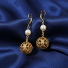 Round Filigree Spear And Faux Pearl Symphony Dangling Earrings on blue fabric