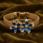 Gold bracelet with blue flower charms on a brown fabric background