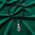 Black beaded necklace with a silver pendant on a green satin background