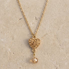 Topaz Pave Crystal Heart Pendant Champagne Bead Drop Necklace 16" + 3" Extension displayed on flat limestone