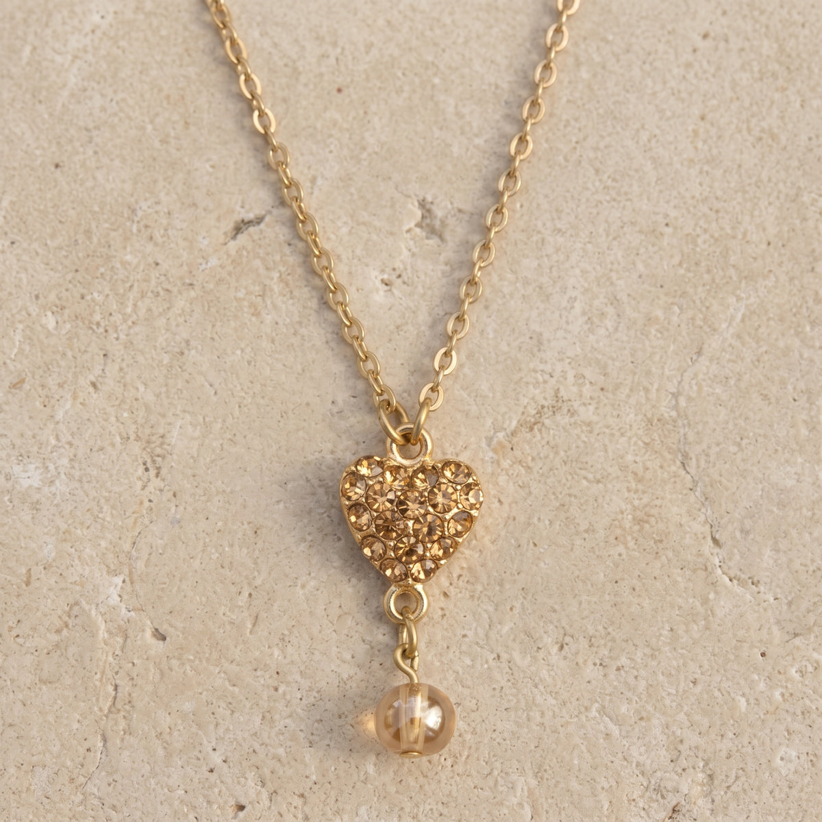 Topaz Pave Crystal Heart Pendant Champagne Bead Drop Necklace 16" + 3" Extension displayed on flat limestone
