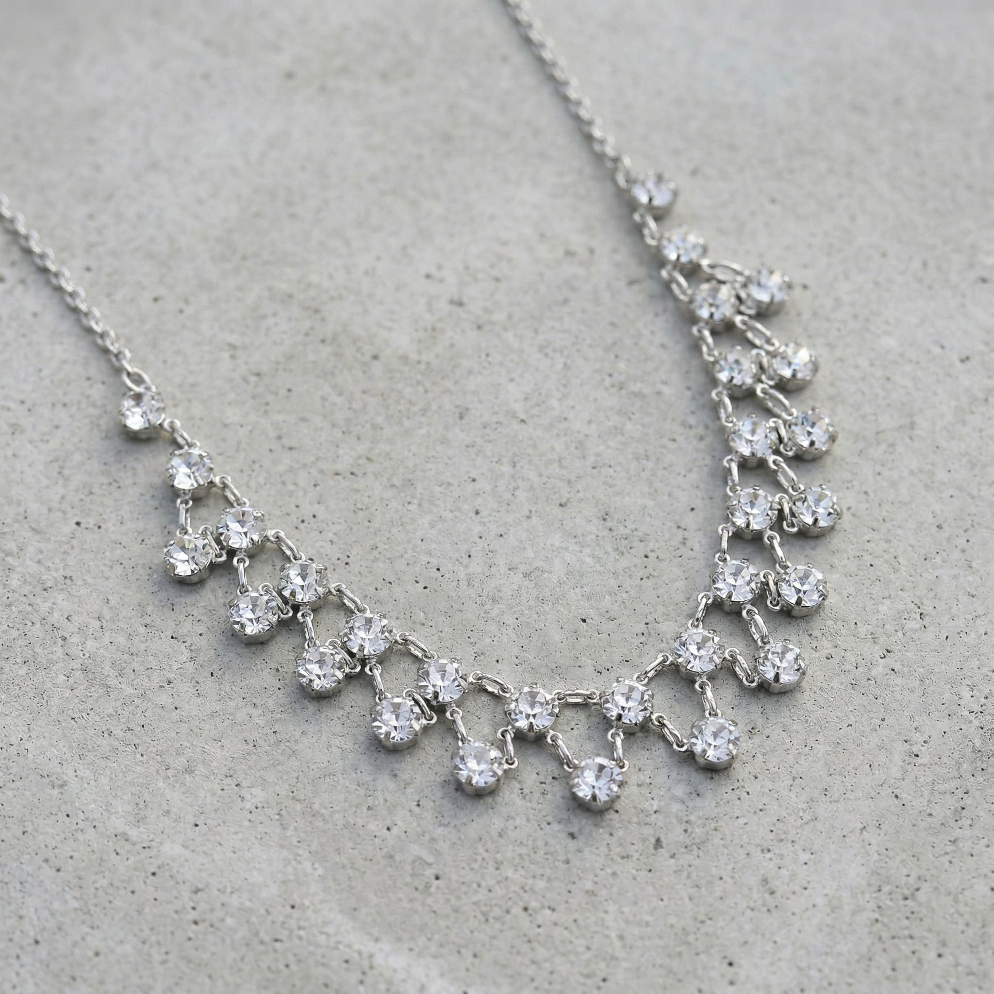 Silver necklace with clear crystals on a gray cement surface