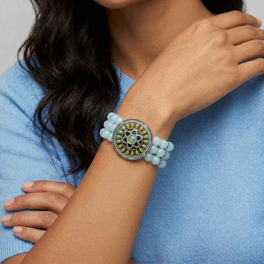 Woman wearing a blue beaded bracelet with a decorative floral center on a gray background