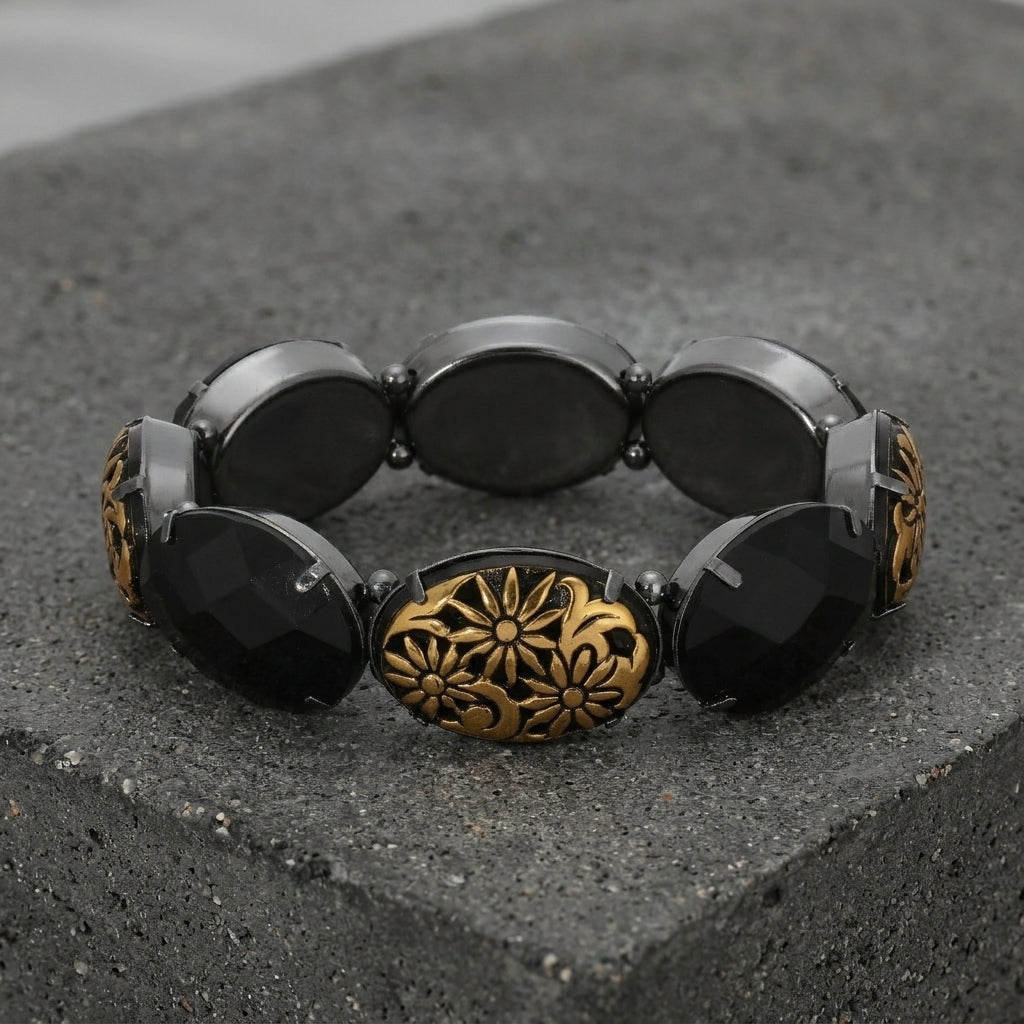 Black beaded bracelet with a gold floral clasp on a dark stone surface