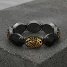 Black beaded bracelet with a gold floral clasp on a dark stone surface