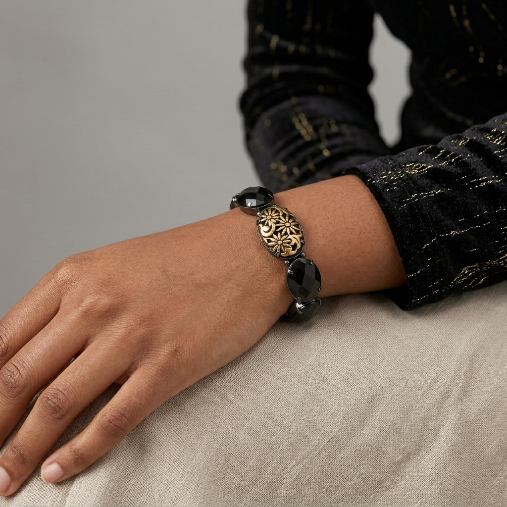 Hand wearing a black and gold bracelet on a neutral background