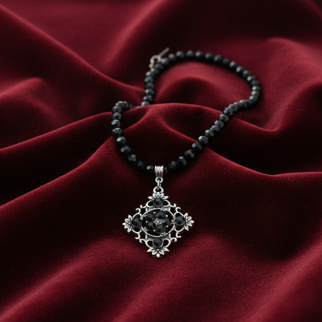 Necklace with black beads and silver pendant on a red fabric background