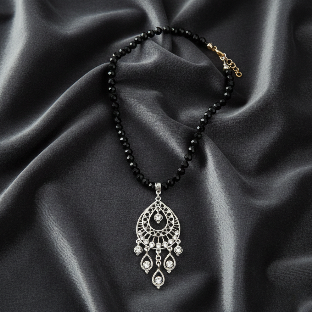 Black beaded necklace with a silver pendant on a black satin background