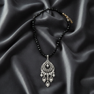 Black beaded necklace with a silver pendant on a black satin background