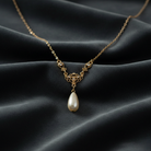 Gold necklace with a pearl pendant on a dark fabric background