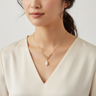 Woman wearing a gold necklace with a pearl pendant against a plain background