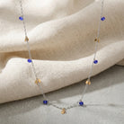 Faceted Blue Bead & Gold Charms Link Necklace on a beige fabric background