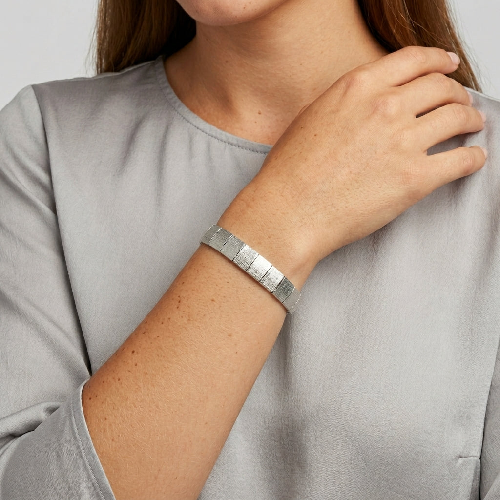Person wearing a silver bracelet on a plain background