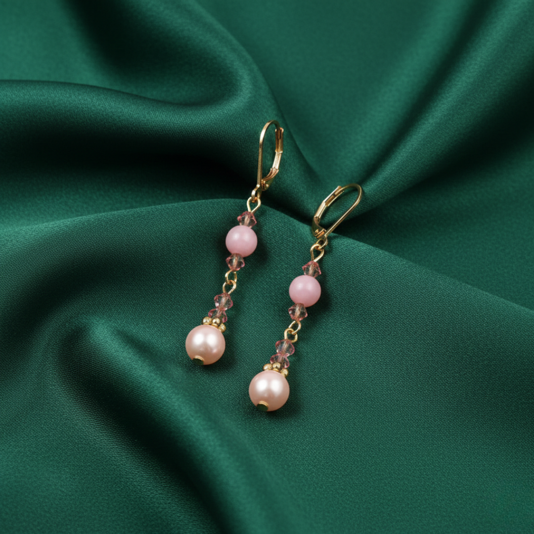 Pair of rose pink faux pearl earrings on a green fabric background