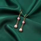 Pair of rose pink faux pearl earrings on a green fabric background