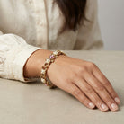 Close-up of a hand wearing a bracelet with pearls and a pink crystals on a neutral background