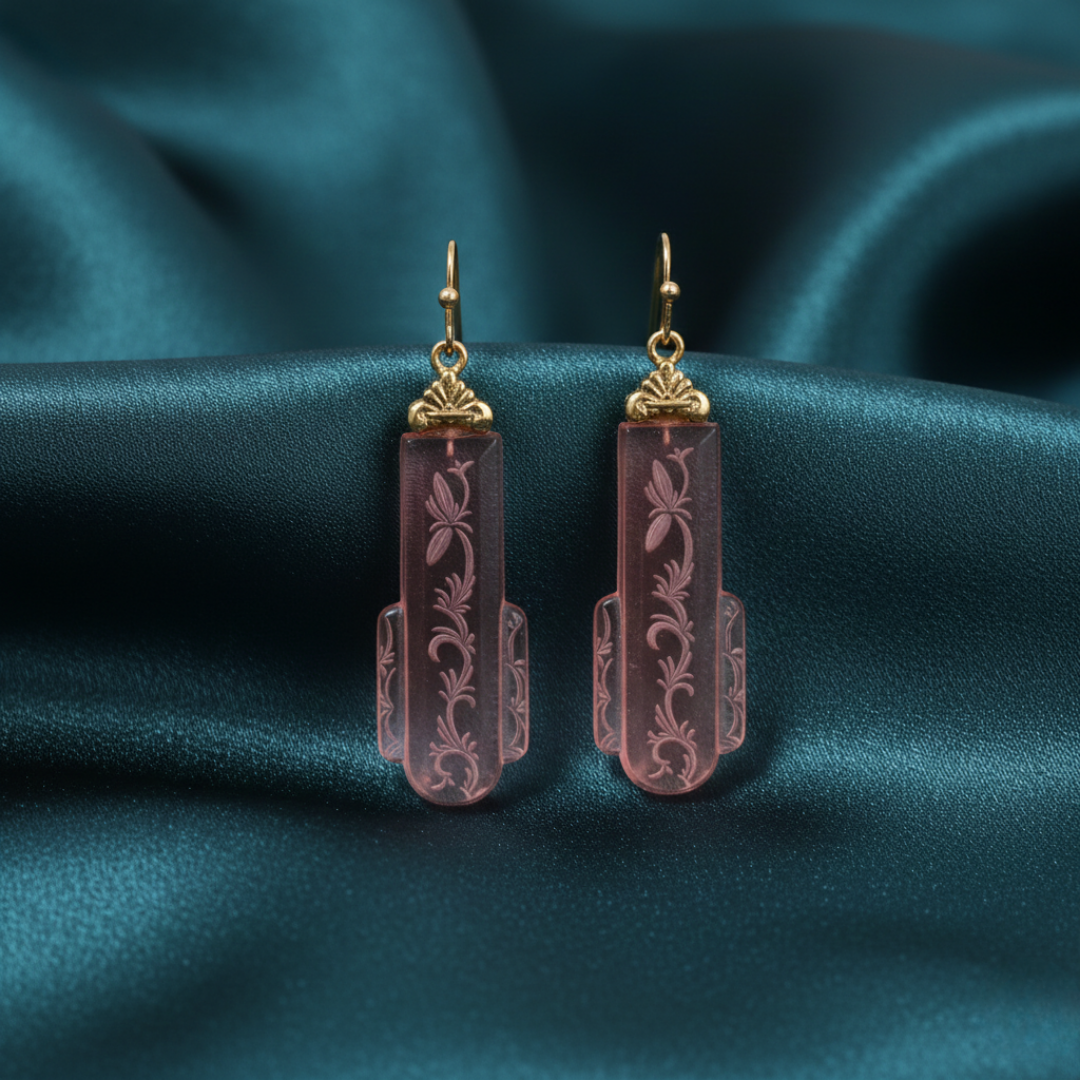 Pair of pink glass earrings with gold accents on a teal fabric background