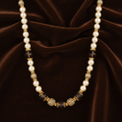 Pearl necklace with gold and black beads on a brown fabric background