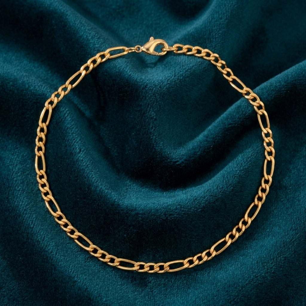 Skinny Gold Figaro Chain Bracelet resting a dark teal fabric
