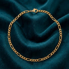 Skinny Gold Figaro Chain Bracelet resting a dark teal fabric
