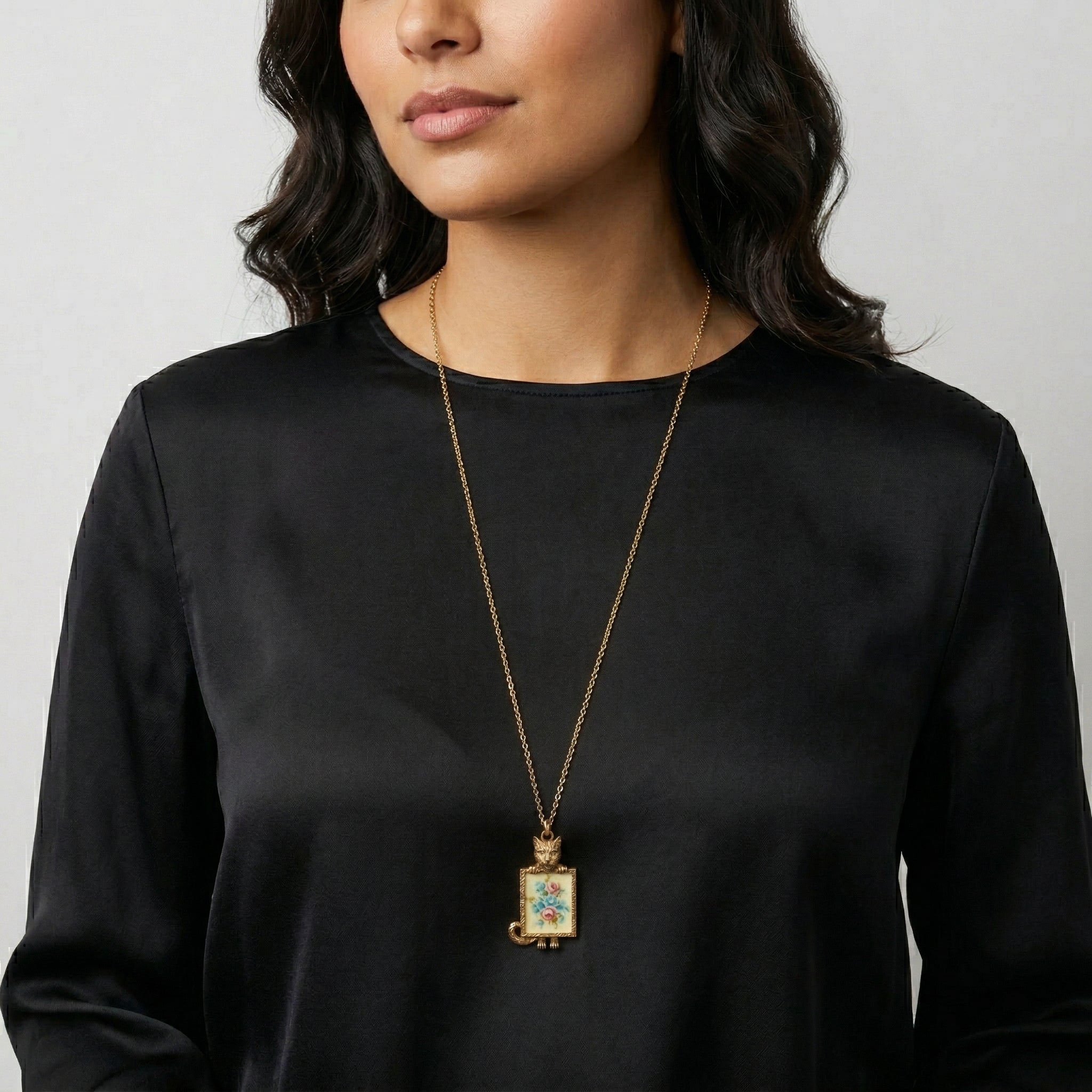 Woman wearing a black top with a gold necklace featuring a cat and floral pendant.