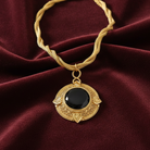 Gold necklace with a black pendant on a maroon fabric background