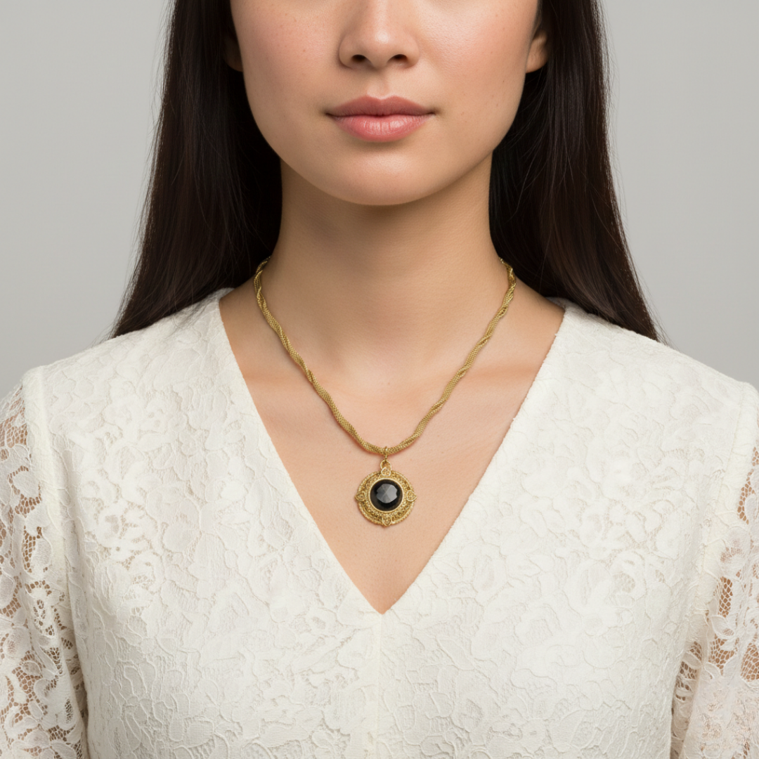 Woman wearing a gold necklace with a black pendant against a gray background