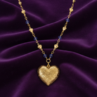 Gold heart-shaped necklace with blue beads on a purple fabric background