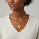 Woman wearing a gold heart-shaped pendant necklace on a neutral background