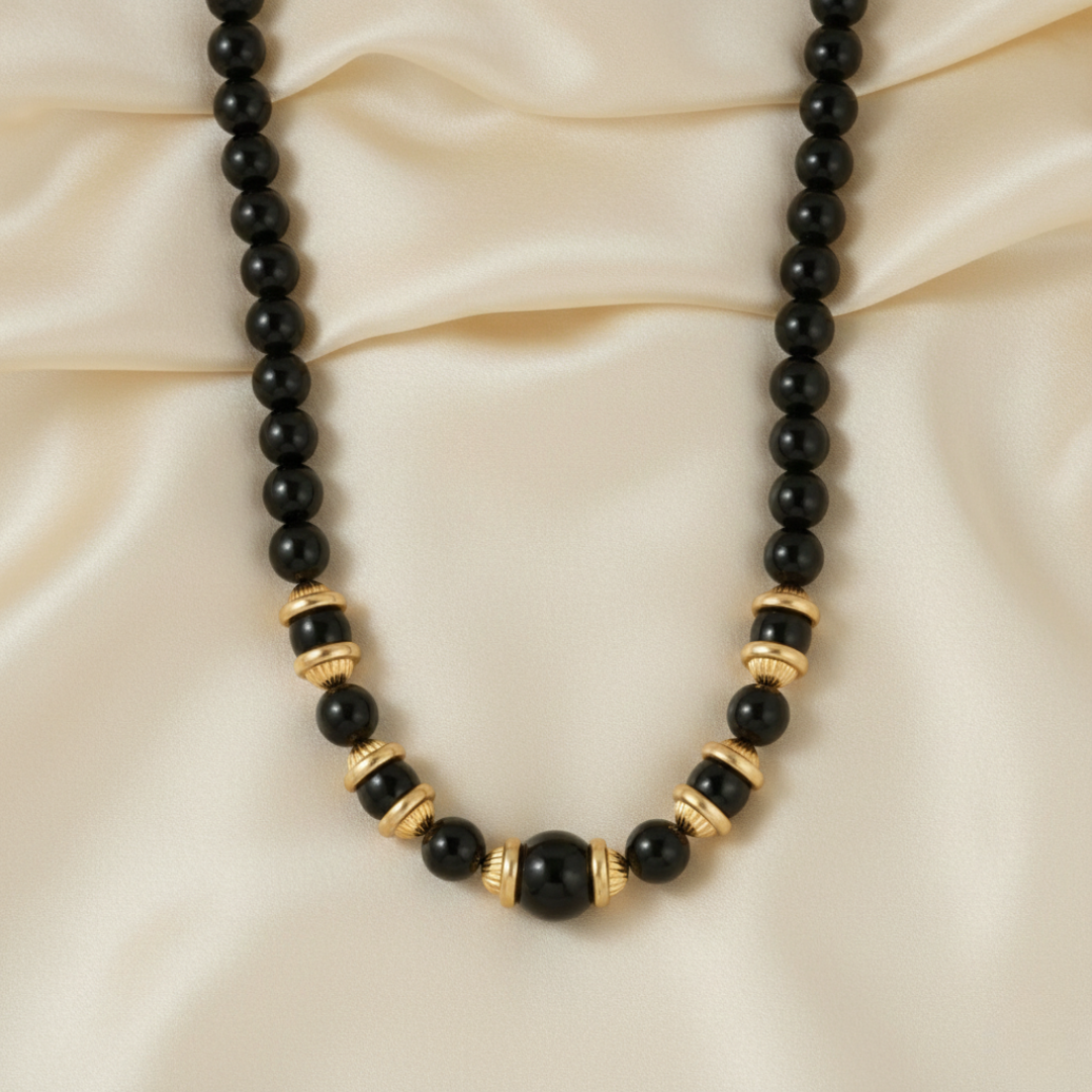 Necklace with black beads and gold accents on a beige fabric background