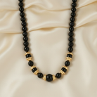 Necklace with black beads and gold accents on a beige fabric background