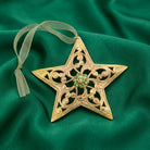 Gold tone Wishing Star Christmas tree ornament with green crystals resting on green fabric 