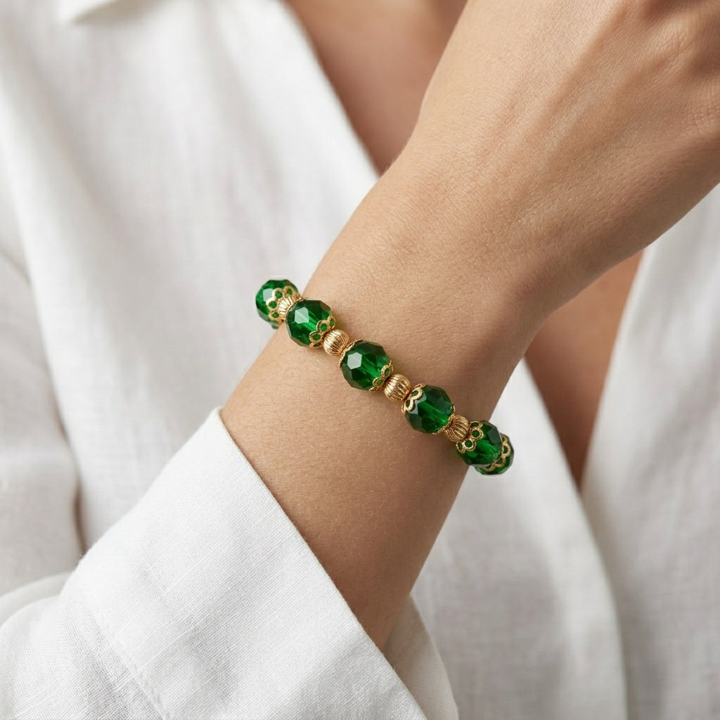 Close up of a woman in a white outfit wearing a green beaded bracelet on her wrist with gold tone accents