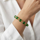 Close up of a woman in a white outfit wearing a green beaded bracelet on her wrist with gold tone accents