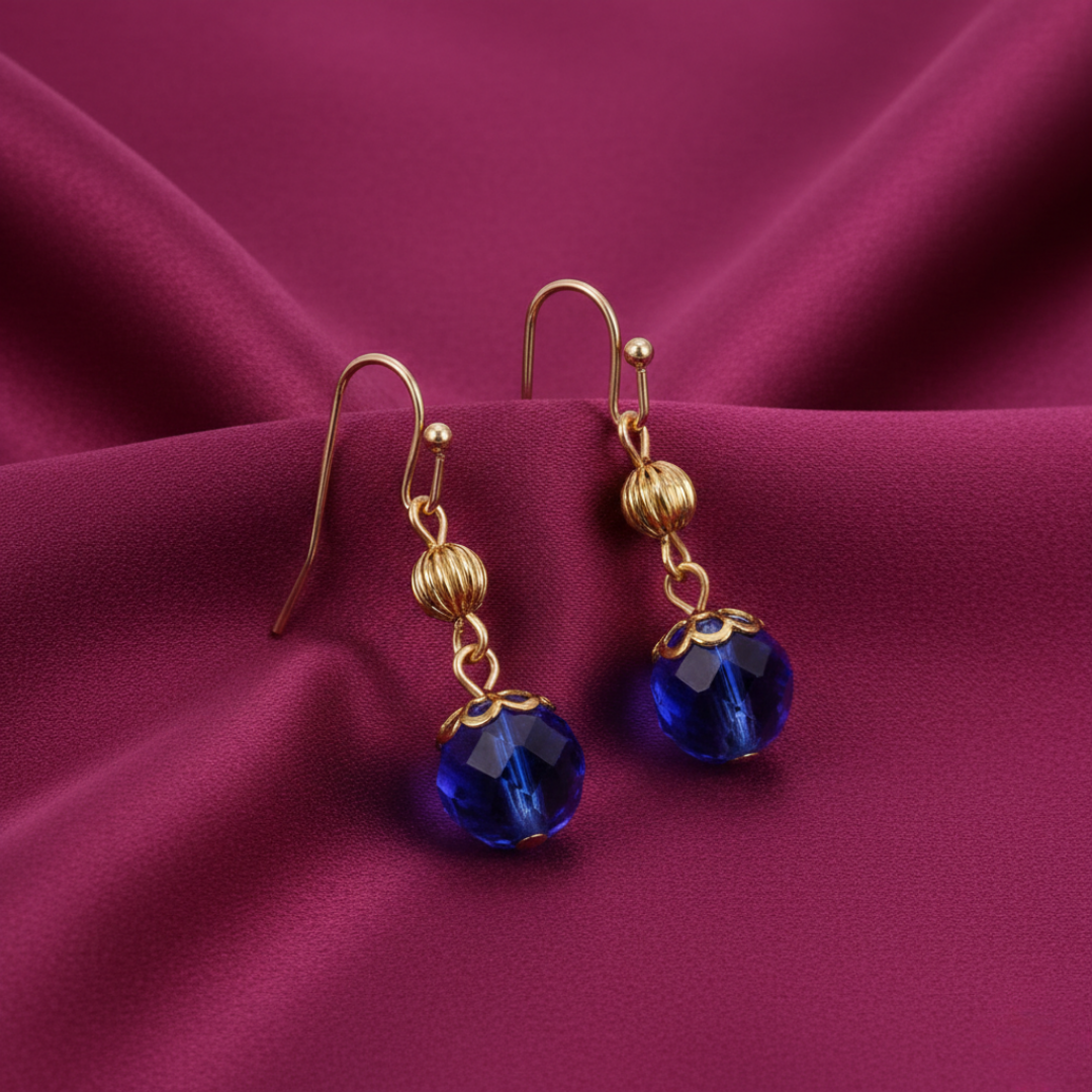 Gold earrings with blue crystals on a purple fabric background