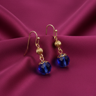 Gold earrings with blue crystals on a purple fabric background