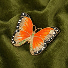 Butterfly-shaped brooch with orange and black wings on a green fabric background