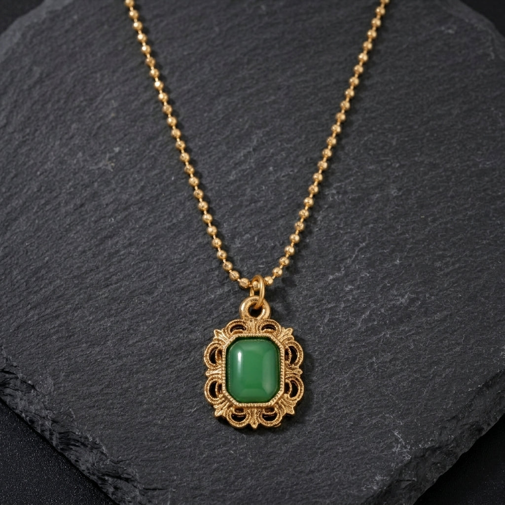 Gold necklace with a green gemstone pendant resting on a black stone surface