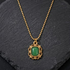 Gold necklace with a green gemstone pendant resting on a black stone surface