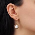 A close-up of a model's ear wearing a White Octagon Moonstone & Gold Filigree Drop Earrings