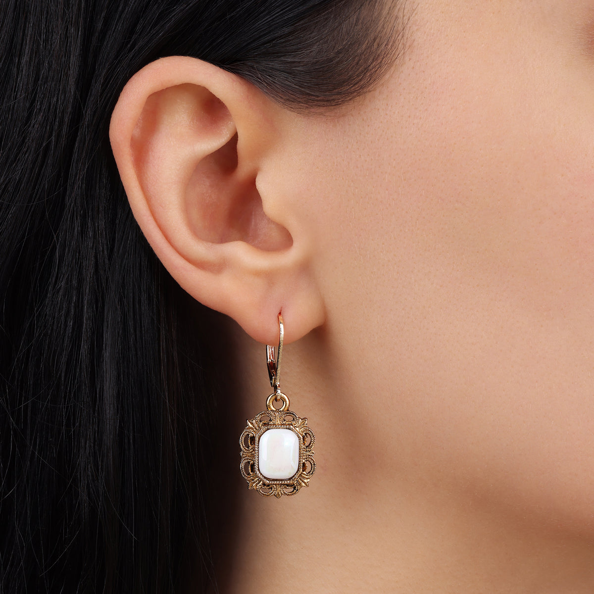 A close-up of a model's ear wearing a White Octagon Moonstone & Gold Filigree Drop Earrings