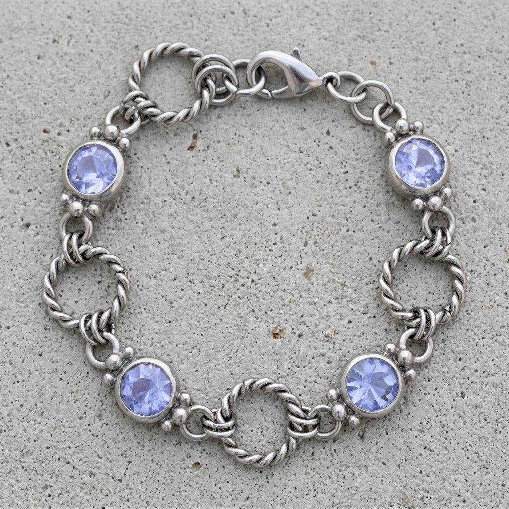 Silver tone twisted rope link bracelet with light sapphire blue crystals resting on a cement surface