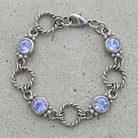 Silver tone twisted rope link bracelet with light sapphire blue crystals resting on a cement surface