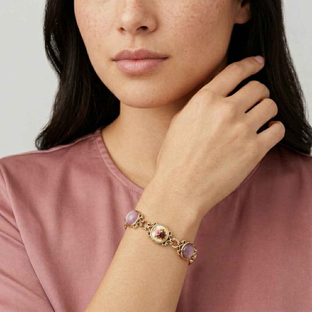 Woman wearing a gold bracelet with cabochon stones and a floral design on a plain background