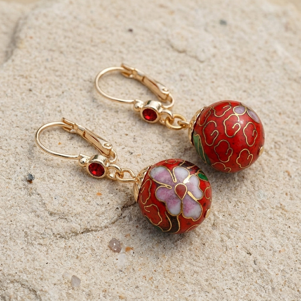 Pair of red and gold earrings on a sandy surface
