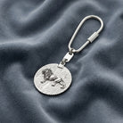 Silver keychain with lion emblem on a textured gray fabric background