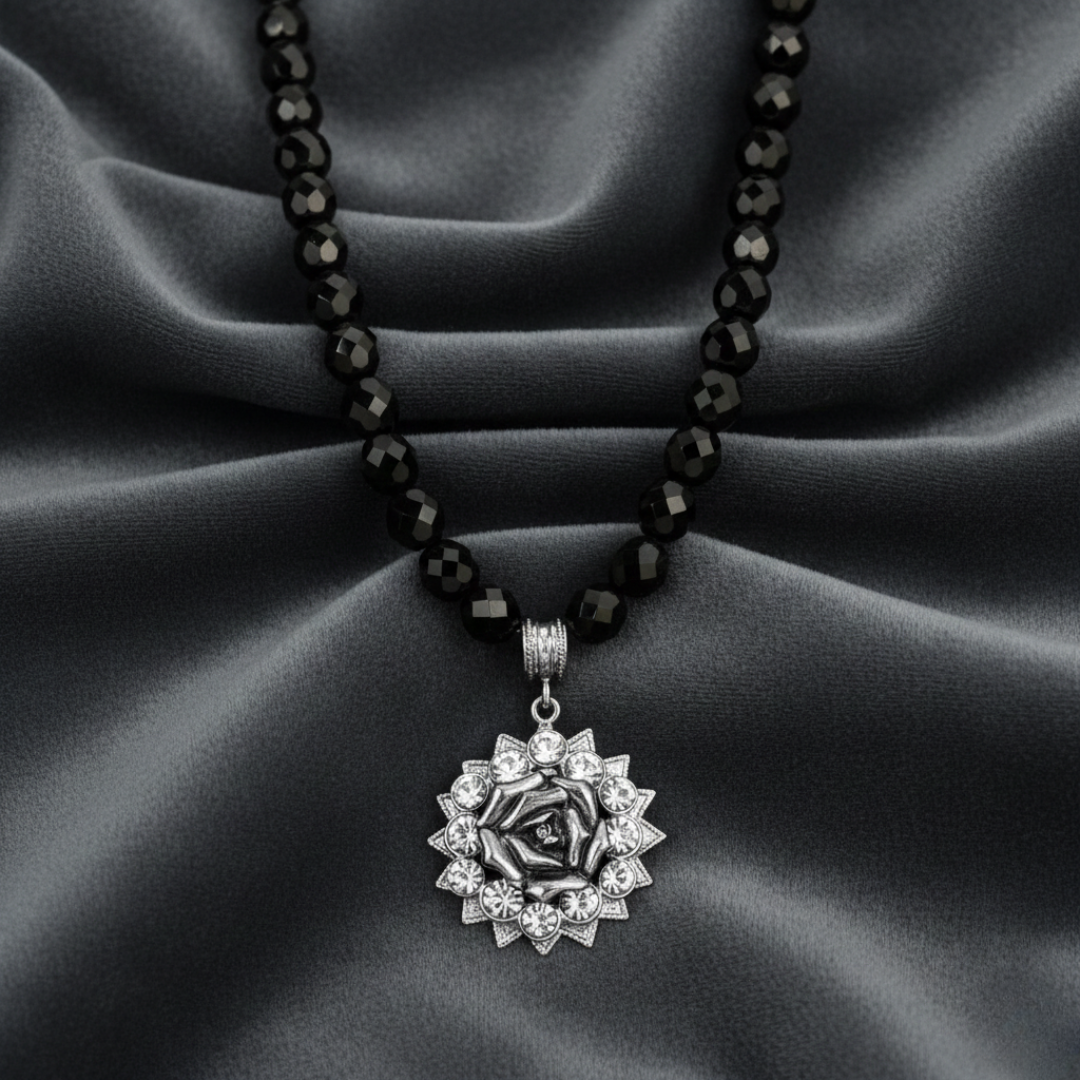 Necklace with a silver pendant on a black beaded chain against a gray fabric background